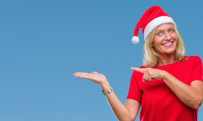 Obraz premium Middle age blonde woman wearing christmas hat over isolated background amazed and smiling to the camera while presenting with hand and pointing with finger.