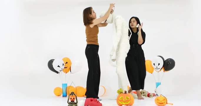 Studio shot of family, two woman and one boy, preparing fancy costume in mummy style for funny activity in christmas festival with colorful balloons and other halloween objects.