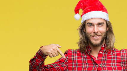 Young handsome man with long hair wearing santa claus hat over isolated background looking confident with smile on face, pointing oneself with fingers proud and happy.