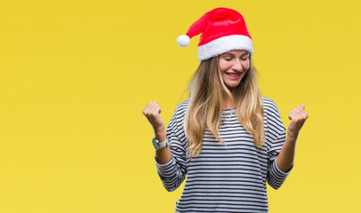 Young beautiful blonde woman wearing christmas hat over isolated background very happy and excited doing winner gesture with arms raised, smiling and screaming for success. Celebration concept.