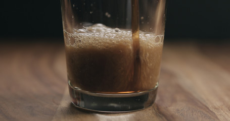 closeup pan of stout beer pour into a glass on wooden table