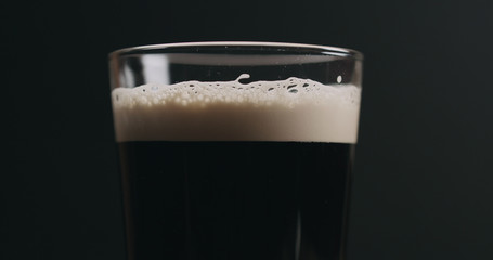 Closeup dark stout beer with bubbles over black background