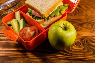 Bottle of water, green apple and lunch box with sandwich, cucumbers and tomatoes on wooden table