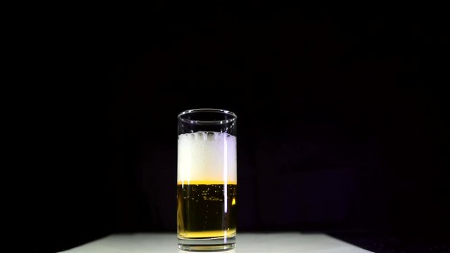 Pouring light beer into a glass beaker in slow motion. Air bubbles rise and create foam. Yellow beer, black background.