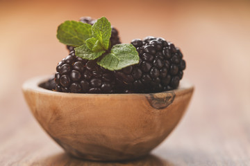 fresh blackberries in wood bowl on wooden table with mint leaves