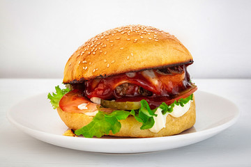 Hot tasty hamburger on a plate on a white background. Homemade hamburger stuffed with beef patties, tomato, pickled cucumber and onion, mayonnaise, ketchup, cheese and salad. Fast food
