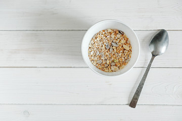 top view healthy breakfast muesli with snacks, white bowl and spoon on white wood background