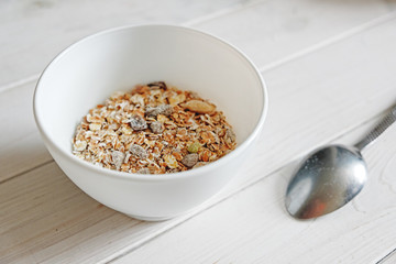 healthy breakfast muesli with snacks, white bowl and spoon on white wood background