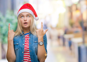 Young caucasian woman wearing christmas hat over isolated background amazed and surprised looking up and pointing with fingers and raised arms.