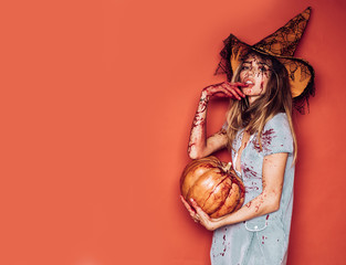 Halloween girl with a carved Pumpkin. Beautiful young surprised woman in costume holding pumpkin. Halloween Witch with pumpkin. Sexy vampire woman with blood on her face. Halloween party art design.