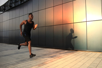 Fototapeta na wymiar Full length of young African man in sports clothing jogging while exercising outdoors, at sunset or sunrise. Runner.