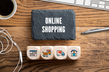 Schiefertafel mit Aufschrift "Online Shopping" und Würfel mit Einkauf-Symbolen am Computer-Arbeitsplatz