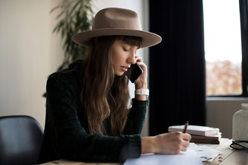 Successful freelancer using smartphone, working from home. Beautiful woman talking on mobile, writing notes