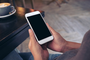 Mockup image of hands holding white mobile phone with blank screen with  coffee cup on table in modern cafe