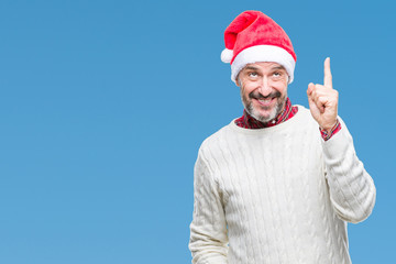 Naklejka premium Middle age hoary senior man wearing christmas hat over isolated background pointing finger up with successful idea. Exited and happy. Number one.