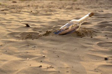 Message in a bottle on the beach, with a letter of distress in the sand on the beach in the summer and warm colors. The female hand takes out bottle with a letter from sea.