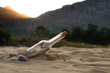 Message in a bottle on the beach, with a letter of distress in the sand on the beach in the summer and warm colors. The female hand takes out bottle with a letter from sea.
