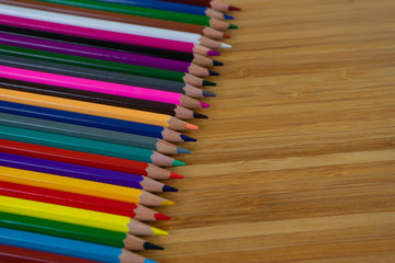 Multi-colored pencils lined up in a row and on brown background.