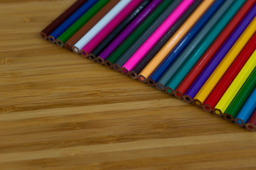 Multi-colored pencils lined up in a row and on brown background.