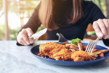 Closeup image of a woman's hand using knife and fork to eat fried chicken and french fries in restaurant