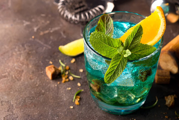 Blue Lagoon cocktail with ice, mint and slice orange on dark stone background, close up