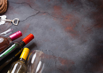 Bottles of red white and pink rose wine with glasses and corkscrew opener on stone kitchen table...