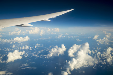 Travel background of clean modern airplane wing over bright blue sky with puffy white clouds