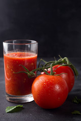 Fresh tomato juice in glass on stone background with water drops on tomatoes. Vegetable drink