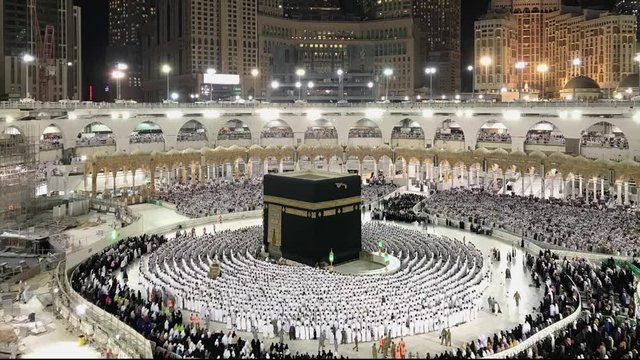 Timelapse of Muslim pilgrims in white ihram cloth from lines facing the Kaaba and perform evening prayer.