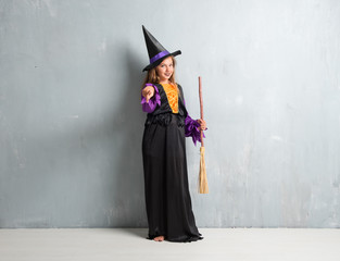 Little girl dressed as a witch for halloween holidays pointing to the front