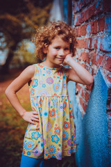 Little caucasian girl posing for a photo against a brick wall. Autumn, orange and gold colors.