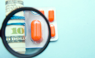 expensive treatment, medicines and money under a magnifying glass on a blue background