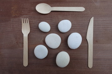 Meal time abstract concept with fork, spoon, knife and stones over wooden board