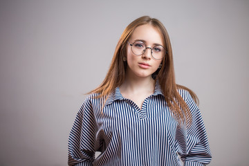 Horizontal portrait of beautiful young woman wearing glasses and shirt on grey background. Student girl