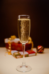Christmas shampagne glass with presents in the background. Glass with bubbles. Christmas balls and decorations. Holiday concept