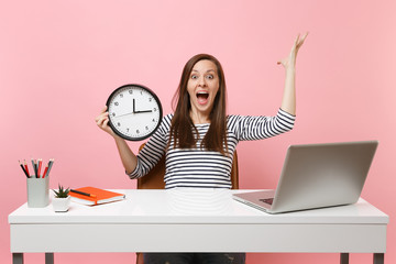 Shocked woman screaming spreading hands holding alarm clock sit, work at office with pc laptop...