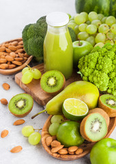 Glass bottle of fresh smoothie juice organic green toned fruit and vegetables on stone kitchen background. With almond nuts in bowl.