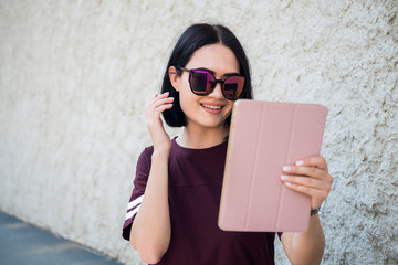 Pretty brunette using a tablet and loking at camera having videocall while chilling outdoors.