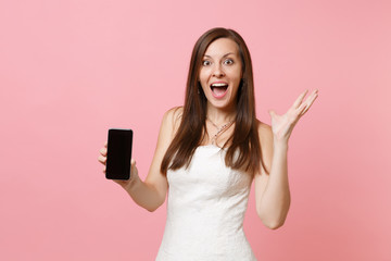 Fototapeta premium Amazed bride woman in wedding dress spreading hands, holding mobile phone with blank black empty screen isolated on pastel pink background. Wedding to do list. Organization of celebration. Copy space.