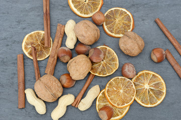 hazelnuts, walnuts, cinnamon  stick, orangen slices and peanuts on black slate
