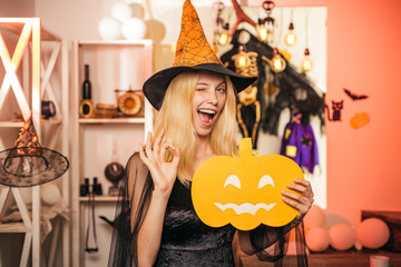 Beautiful young surprised woman in witches hat and costume holding pumpkin. Surprised woman in...