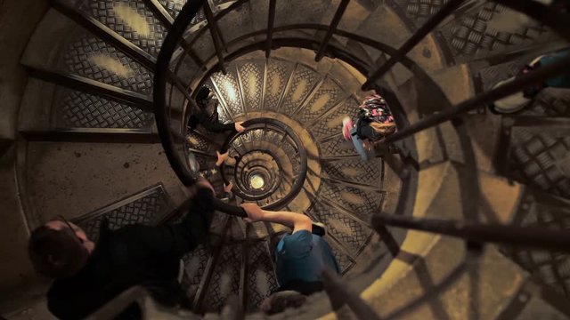 Unrecognizable people tourists climb the high spiral staircase up. Hold onto the railing with their hands. The concept of business growth with obstacles. top view slow motion.