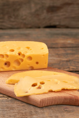 Slices of Maasdam cheese on cutting board. Fresh tasty swiss cheese on rustic wooden background.