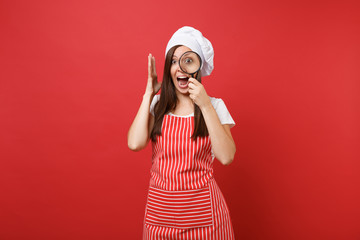 Housewife female chef cook or baker in striped apron white t-shirt toque chefs hat isolated on red wall background. Housekeeper woman hold and look through magnifying glass. Mock up copy space concept