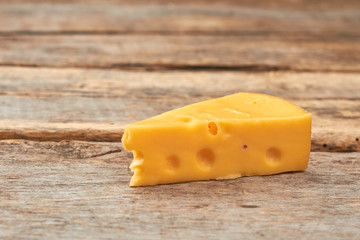 Piece of swiss cheese on wooden background. Dutch cheese with holes on rustic wooden boards. Delicious dairy product.