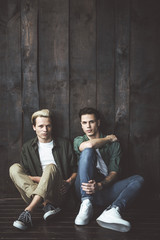 Toned portrait of two handsome guys posing against the wooden wall. They looking at camera with serious expressions