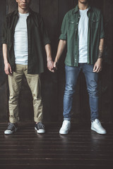 Very special bond. Cropped portrait of two young guys holding hands while standing on wooden background