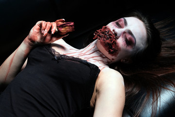 A girl with her eyes closed in a Halloween make-up lies on a black leather sofa, holding a dry red...