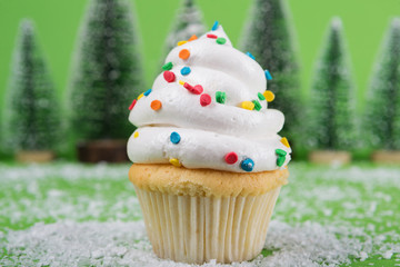 minimal concept, a white cream cupcake decorated with red stars, in the background a lot of decorative Christmas trees and artificial snow