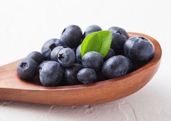 Fresh raw organic blueberries with leaf on wooden spoon on white background. Food concept.